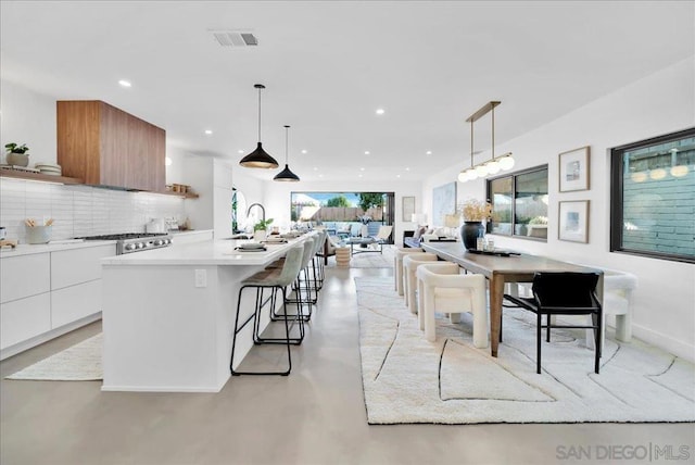 kitchen featuring pendant lighting, a kitchen island with sink, decorative backsplash, and white cabinets