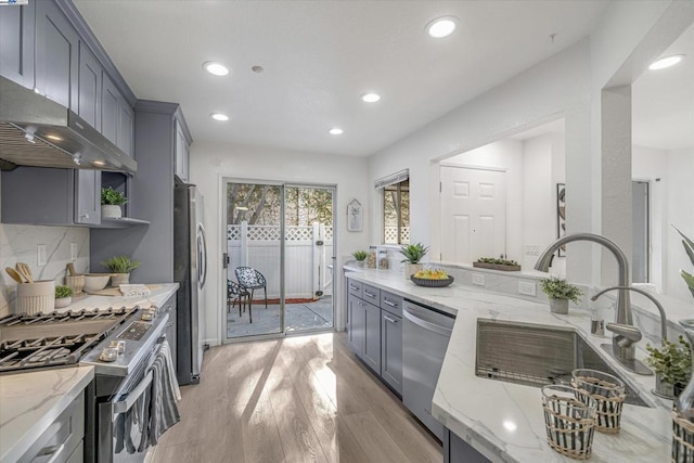 kitchen featuring wall chimney range hood, light stone countertops, sink, and appliances with stainless steel finishes