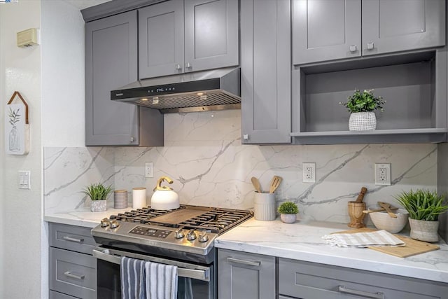 kitchen with gray cabinetry, stainless steel range with gas stovetop, light stone counters, and wall chimney exhaust hood