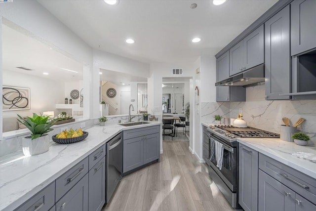 kitchen featuring light stone counters, stainless steel appliances, sink, and gray cabinetry