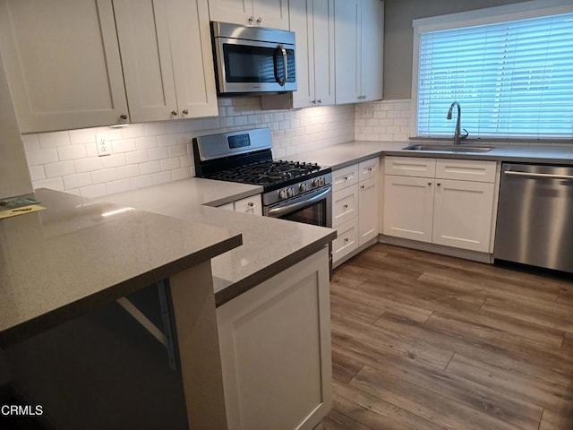 kitchen with appliances with stainless steel finishes, wood-type flooring, sink, white cabinets, and decorative backsplash