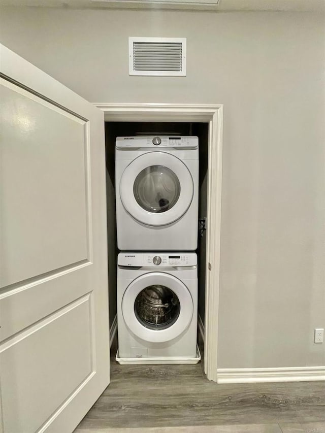 washroom with hardwood / wood-style flooring and stacked washing maching and dryer