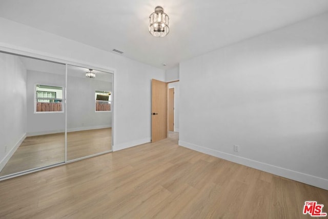 unfurnished bedroom with a chandelier, light hardwood / wood-style floors, and a closet