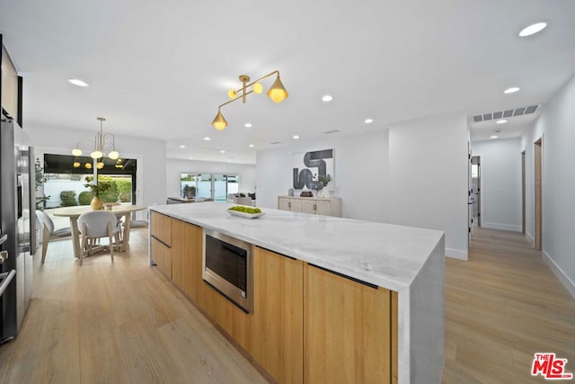 kitchen with built in microwave, light stone countertops, hanging light fixtures, and light wood-type flooring