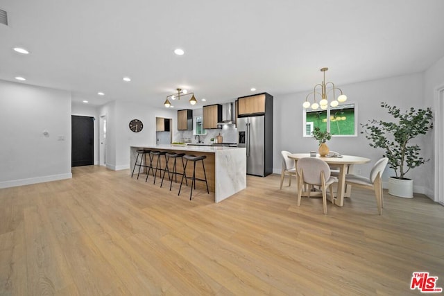 kitchen with light wood-type flooring, high quality fridge, a kitchen breakfast bar, pendant lighting, and wall chimney range hood