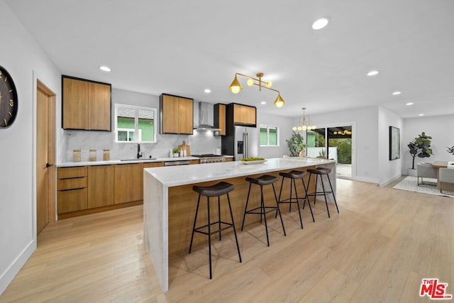 kitchen with a kitchen bar, appliances with stainless steel finishes, pendant lighting, a large island, and wall chimney range hood