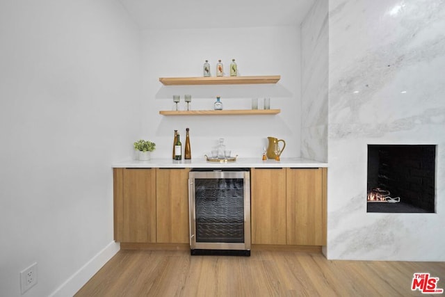 bar with wine cooler, light wood-type flooring, and a fireplace