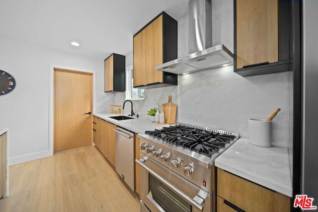 kitchen with wall chimney range hood, sink, backsplash, stainless steel appliances, and light wood-type flooring