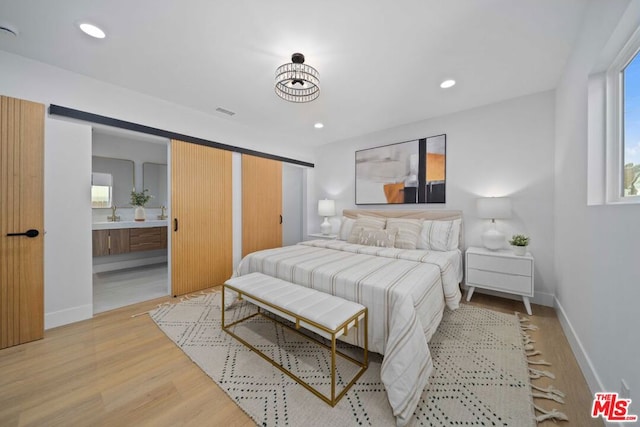 bedroom with connected bathroom, light hardwood / wood-style flooring, and a barn door