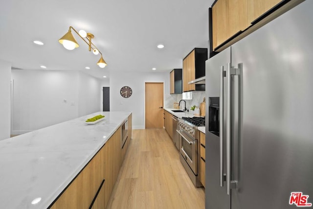 kitchen with light stone counters, sink, light hardwood / wood-style flooring, and premium appliances