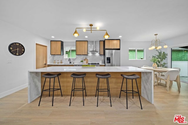 kitchen featuring backsplash, wall chimney exhaust hood, a kitchen bar, and stainless steel fridge with ice dispenser