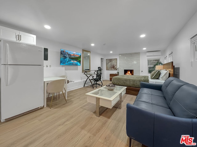 living room featuring a high end fireplace, a wall mounted air conditioner, and light wood-type flooring