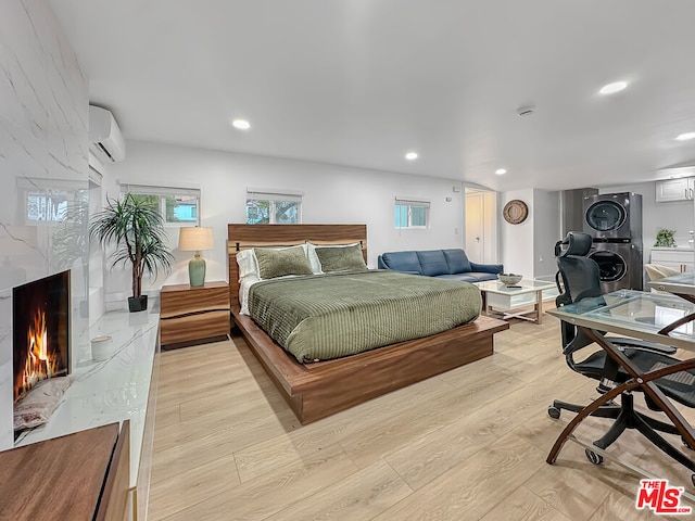 bedroom featuring stacked washer and clothes dryer, a high end fireplace, a wall mounted air conditioner, and light hardwood / wood-style flooring