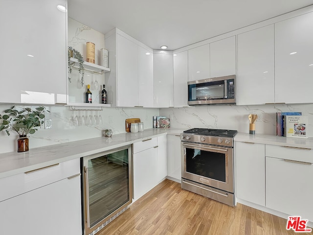 kitchen with appliances with stainless steel finishes, light hardwood / wood-style floors, white cabinets, decorative backsplash, and beverage cooler