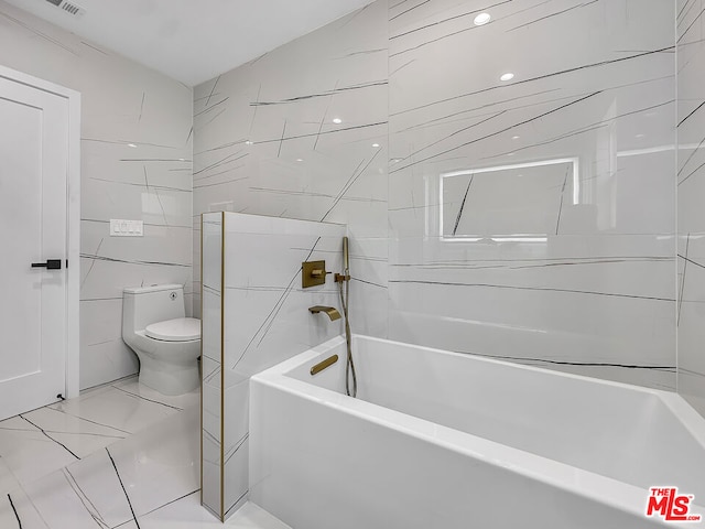 bathroom with tile walls, a tub to relax in, and toilet