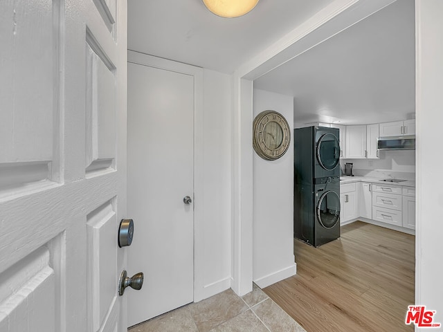 clothes washing area featuring stacked washer / drying machine, light hardwood / wood-style floors, and cabinets