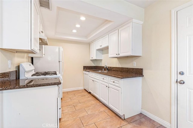 kitchen featuring sink, a raised ceiling, white appliances, dark stone counters, and white cabinets