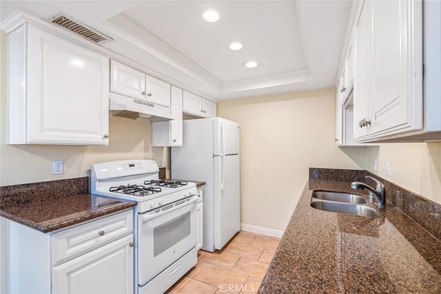 kitchen featuring a raised ceiling, dark stone countertops, white cabinets, and white appliances