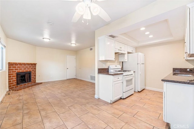 kitchen featuring sink, a brick fireplace, a tray ceiling, white appliances, and white cabinets