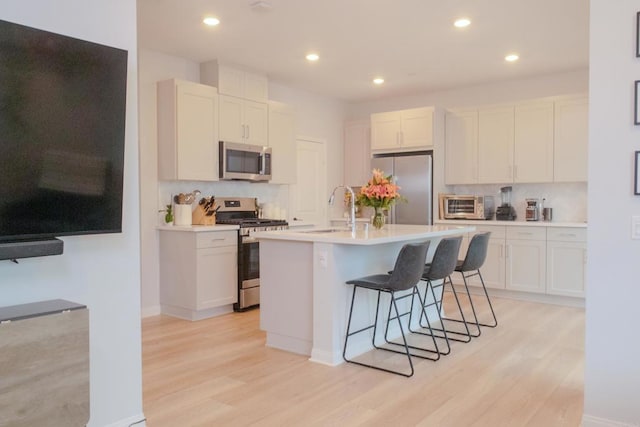 kitchen featuring a breakfast bar, white cabinetry, sink, stainless steel appliances, and a center island with sink