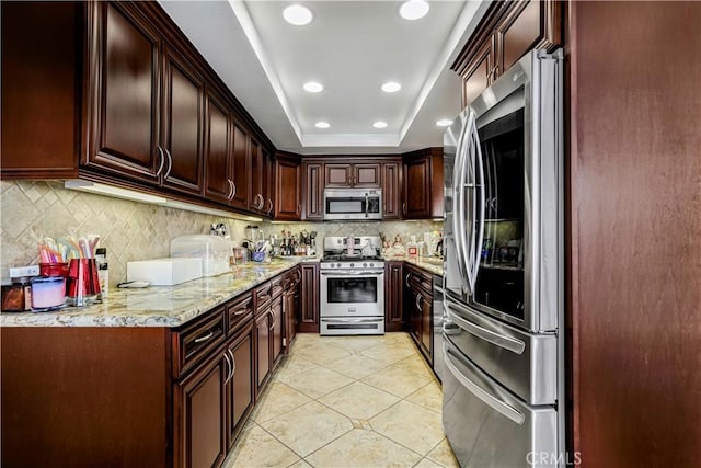 kitchen featuring light tile patterned flooring, backsplash, light stone counters, a tray ceiling, and stainless steel appliances