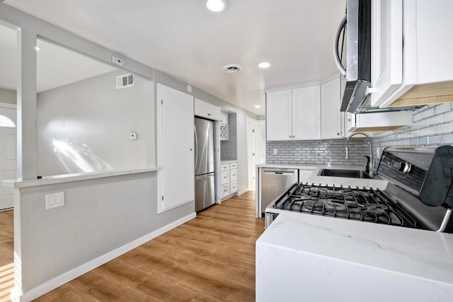 kitchen with appliances with stainless steel finishes, white cabinetry, sink, decorative backsplash, and light stone countertops