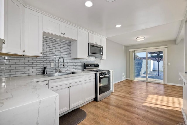 kitchen with white cabinetry, sink, backsplash, stainless steel appliances, and light stone countertops