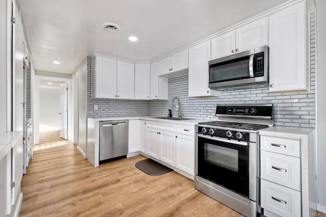 kitchen featuring light countertops, decorative backsplash, appliances with stainless steel finishes, light wood-style floors, and a sink