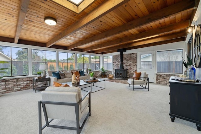 carpeted living room with beam ceiling, a skylight, brick wall, wooden ceiling, and a wood stove