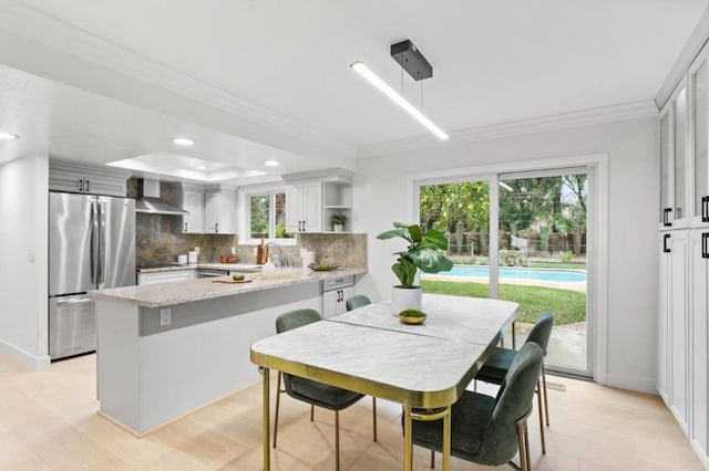 kitchen with stainless steel fridge, white cabinetry, backsplash, light stone counters, and wall chimney exhaust hood