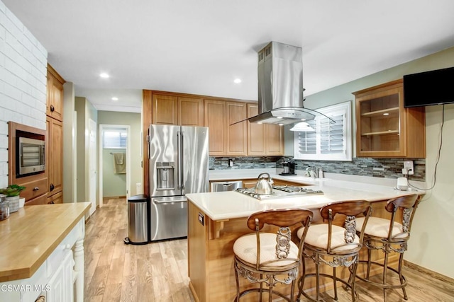 kitchen with island exhaust hood, appliances with stainless steel finishes, a breakfast bar, and light wood-type flooring