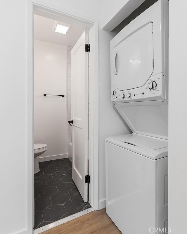 laundry area featuring stacked washer and clothes dryer and dark wood-type flooring