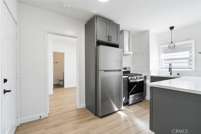 kitchen with hanging light fixtures, gray cabinets, stainless steel appliances, light hardwood / wood-style floors, and wall chimney range hood