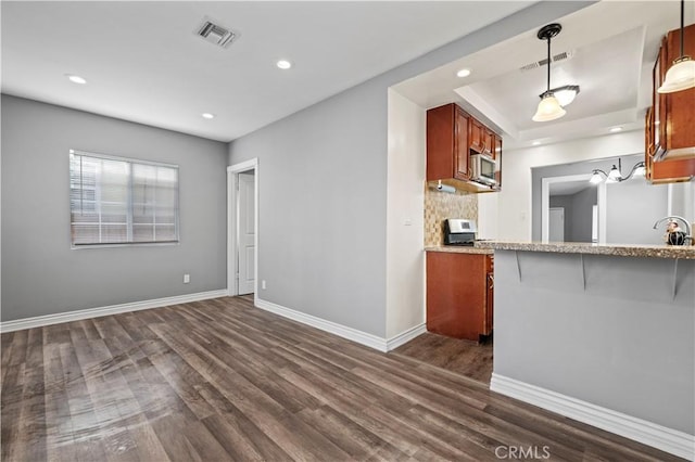 kitchen with pendant lighting, dark wood-type flooring, tasteful backsplash, a kitchen bar, and kitchen peninsula