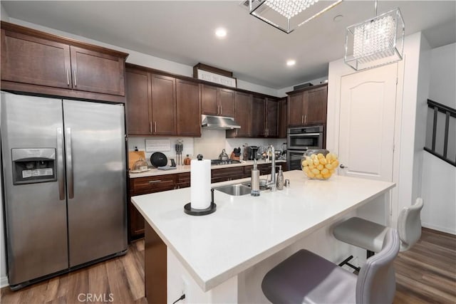 kitchen with dark brown cabinetry, sink, a center island with sink, hardwood / wood-style flooring, and stainless steel appliances