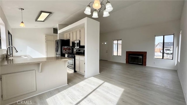 kitchen with decorative light fixtures, sink, kitchen peninsula, stainless steel appliances, and light wood-type flooring