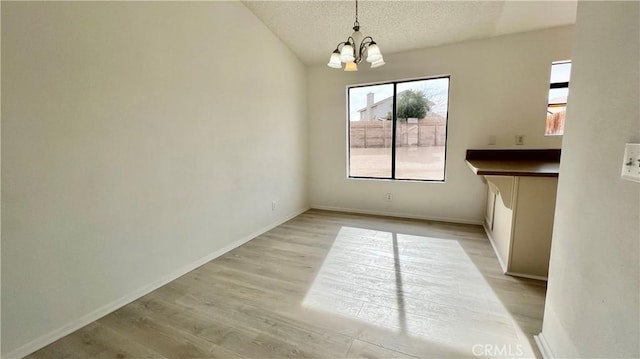 unfurnished dining area with a chandelier, a textured ceiling, and light wood-type flooring