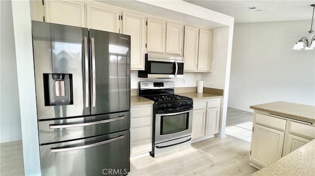 kitchen with appliances with stainless steel finishes, pendant lighting, cream cabinets, a textured ceiling, and light wood-type flooring