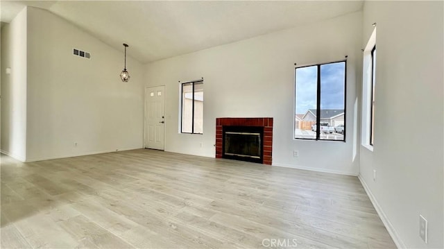 unfurnished living room with high vaulted ceiling, a brick fireplace, a wealth of natural light, and light wood-type flooring