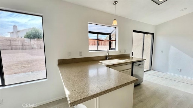 kitchen with sink, decorative light fixtures, light hardwood / wood-style flooring, stainless steel dishwasher, and kitchen peninsula