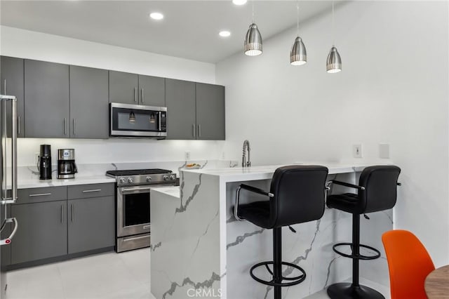 kitchen with appliances with stainless steel finishes, a kitchen breakfast bar, a peninsula, gray cabinets, and pendant lighting