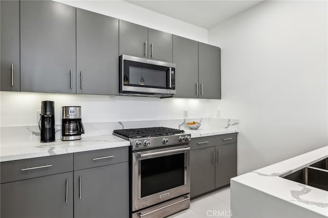 kitchen featuring stainless steel appliances, light stone counters, gray cabinetry, and modern cabinets