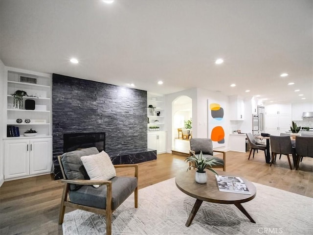 living room with a fireplace, built in shelves, and wood-type flooring