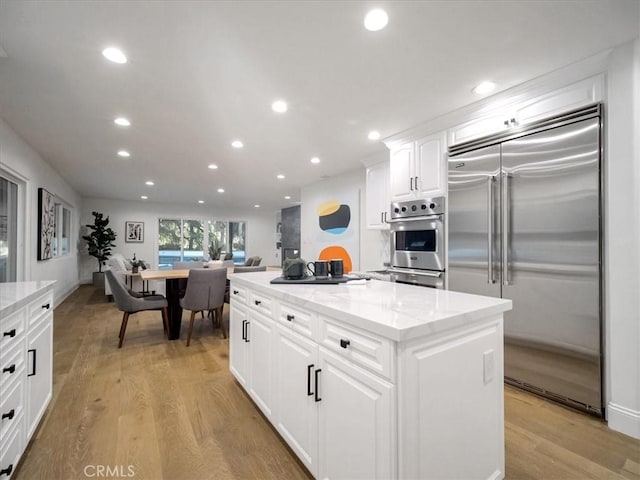 kitchen with stainless steel appliances, a center island, white cabinets, and light wood-type flooring