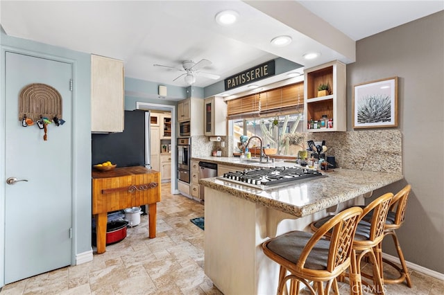 kitchen featuring appliances with stainless steel finishes, sink, backsplash, a kitchen breakfast bar, and ceiling fan