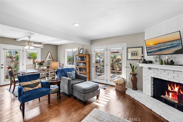 living room featuring ceiling fan, beam ceiling, hardwood / wood-style floors, and a brick fireplace