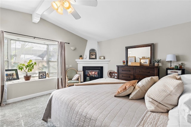 carpeted bedroom with ceiling fan, a large fireplace, and lofted ceiling with beams