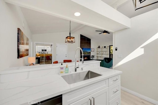 kitchen with sink, light stone counters, lofted ceiling with beams, hanging light fixtures, and white cabinets