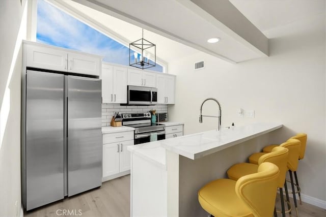 kitchen with white cabinets, a kitchen breakfast bar, hanging light fixtures, kitchen peninsula, and stainless steel appliances