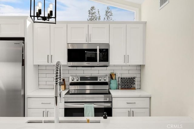 kitchen with white cabinetry, backsplash, stainless steel appliances, and light stone countertops